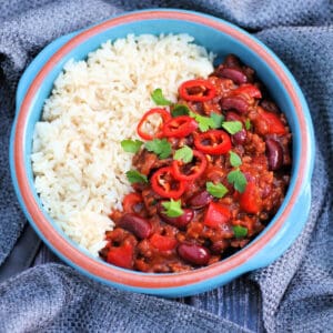 Overhead view of bowl of chilli and rice on grey fabric.