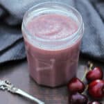 Jar of pink cherry curd with grey background.