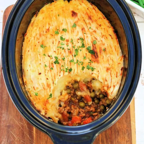 Shepherds pie in slow cooker pot, garnished with herbs.