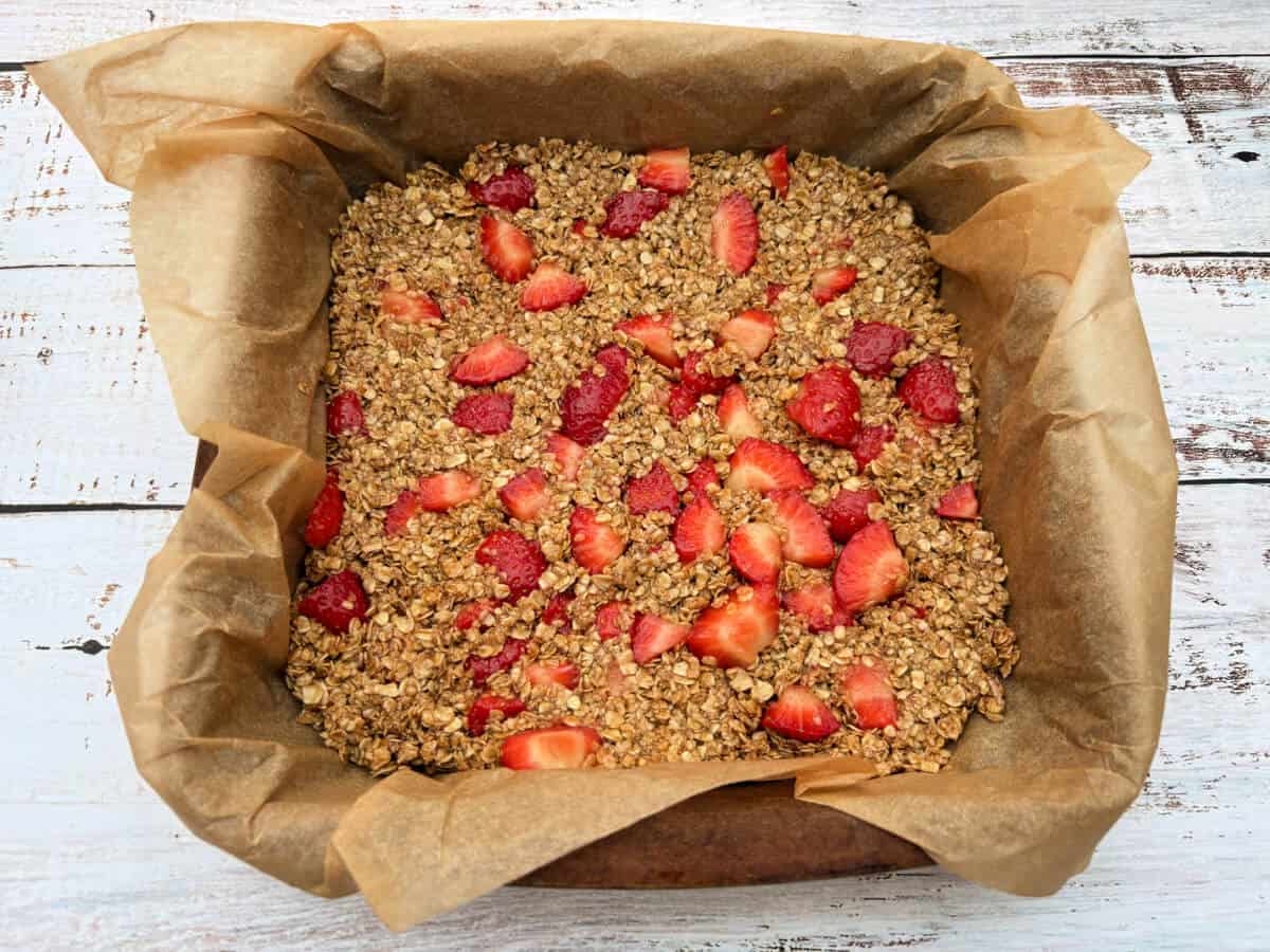 A brown paper-lined baking tray filled with oat mixture and strawberries.