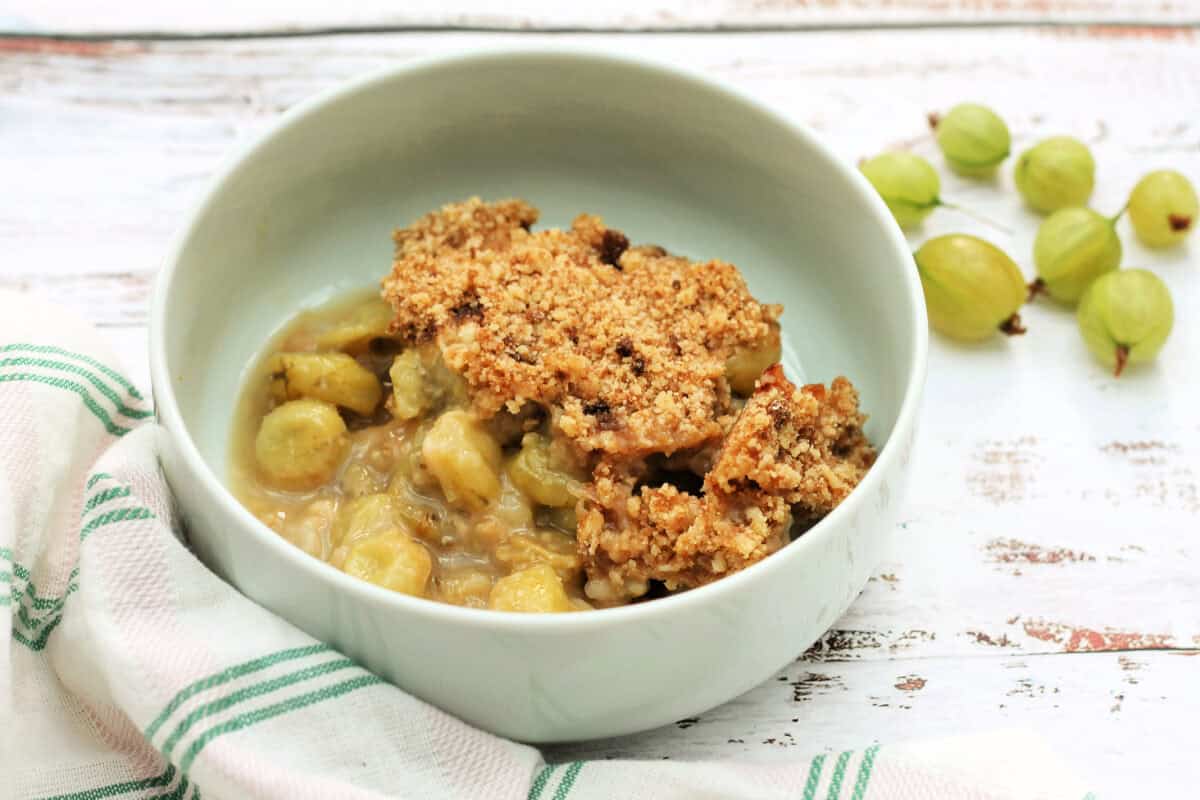 Bowl of gooseberry crumble with cloth in front.
