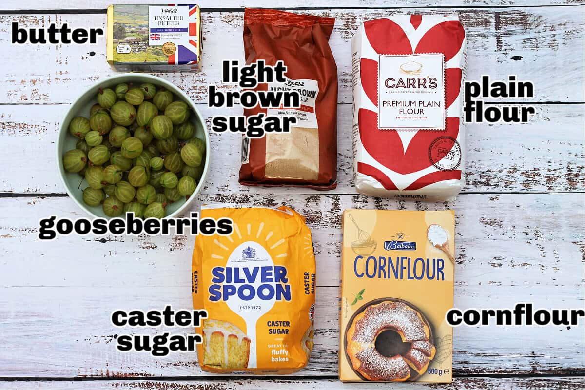 Ingredients for gooseberry crumble on white table with text labels.