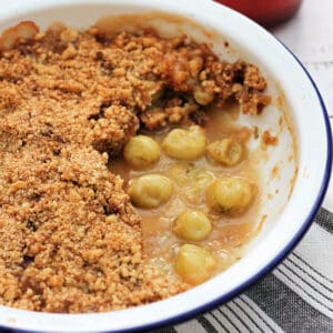 Gooseberry crumble in white pie dish, one portion served.