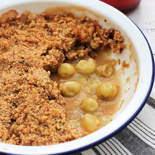 Gooseberry crumble in white pie dish, one portion served.