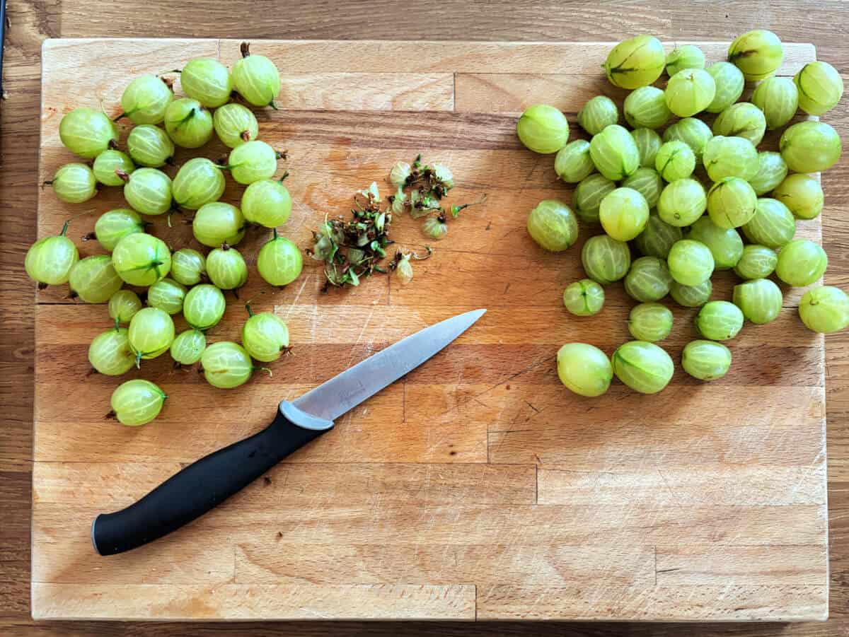 Topping and tailing gooseberries on a wooden board.