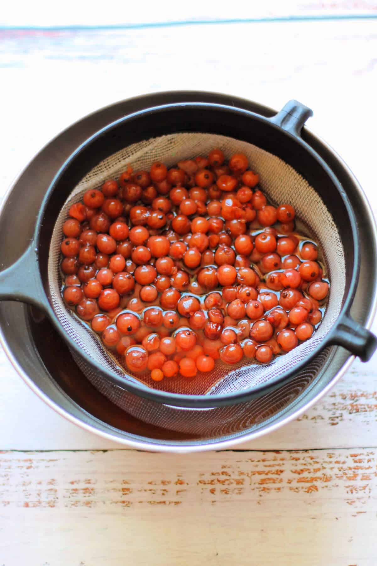Redcurrants in a sieve, over a metal bowl.