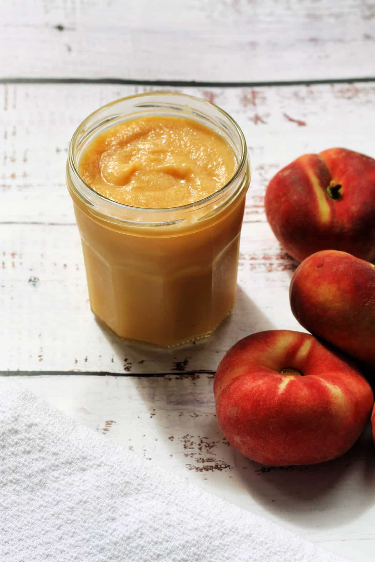 Open jar of fruit curd with peaches to the right.