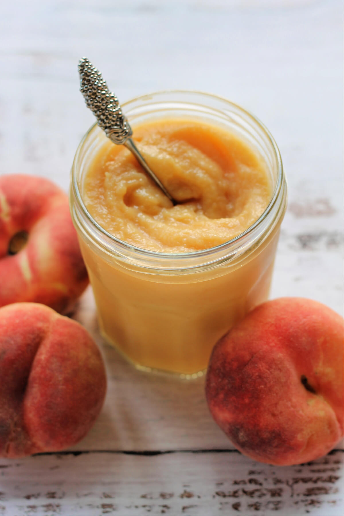 Jar of curd with spoon, peaches around.