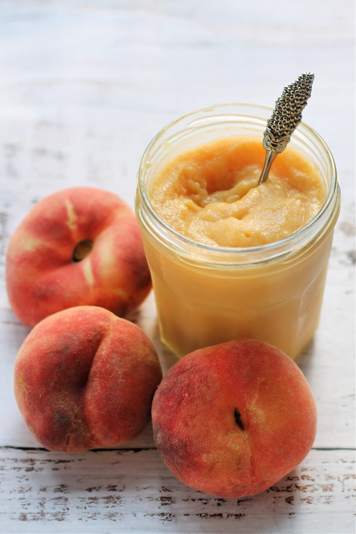 Jar of curd with a spoon in it, with peaches to the side.