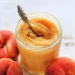 Jar of curd with spoon, peaches next to it.
