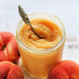 Jar of curd with spoon, peaches next to it.