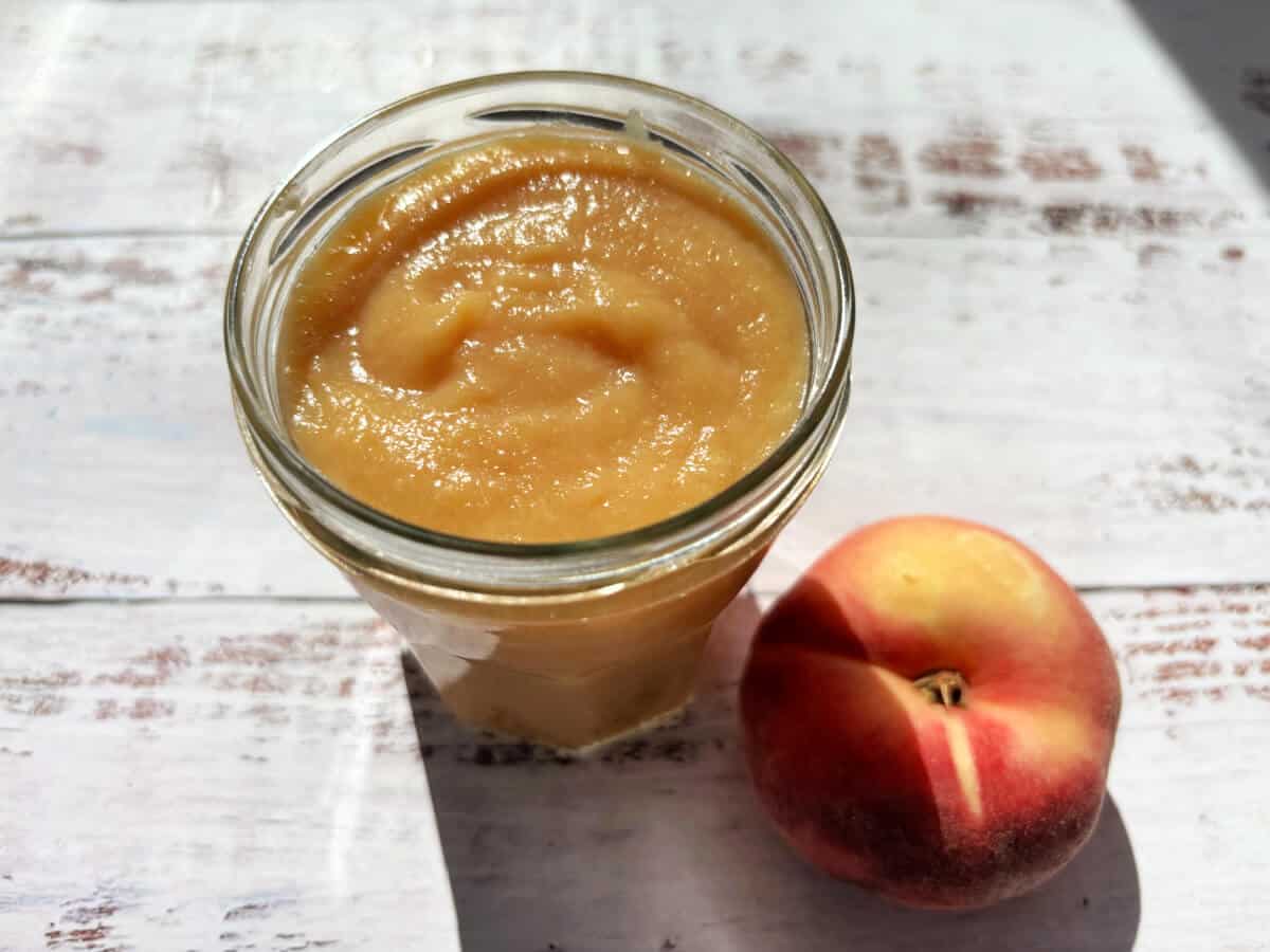 Jar of peach curd with a peach next to it.
