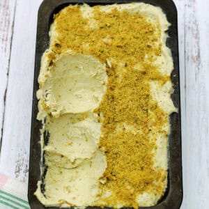 Pistachio ice cream in a container with a few scoops scraped out.