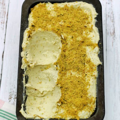Pistachio ice cream in a container with a few scoops scraped out.