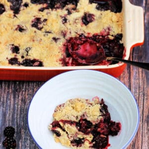 Bowl of blackberry crumble, serving dish with crumble behind.