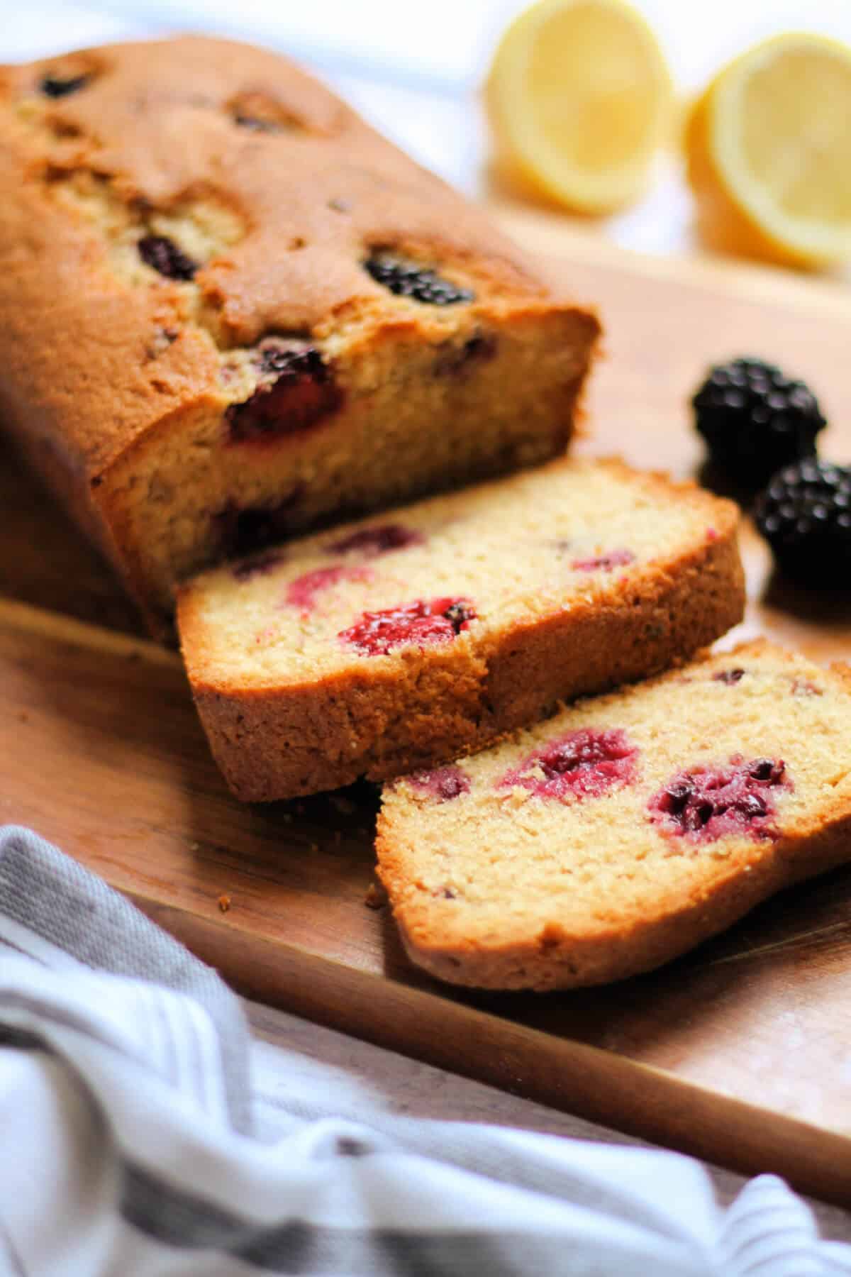 Loaf cake on a wooden board, slices cut showing fruit inside.