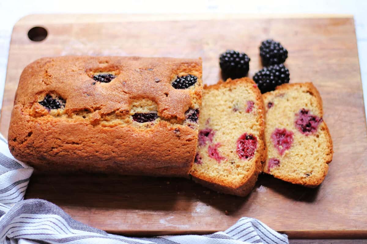 Loaf cake on a board with blackberries to the side.