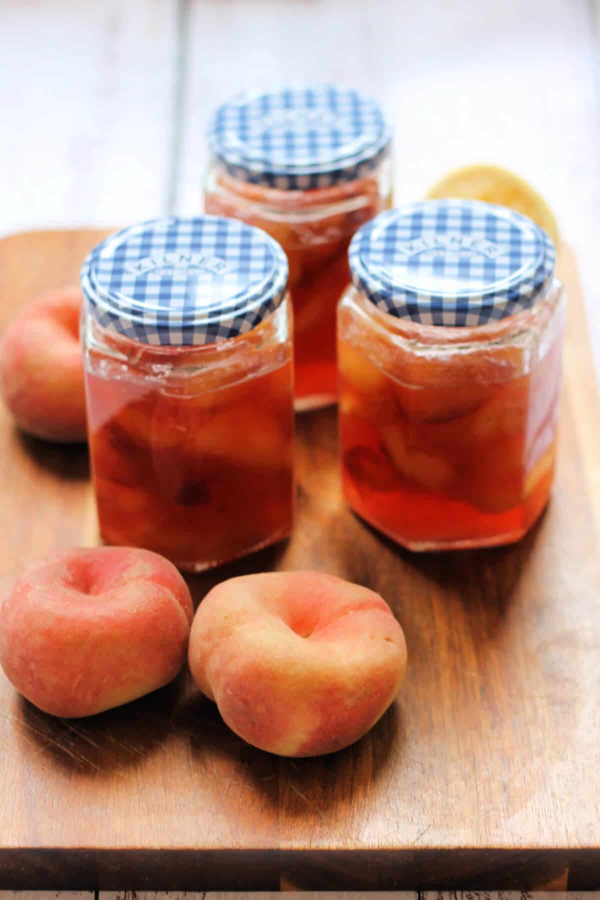 Jars of jam with flat peaches beside them.