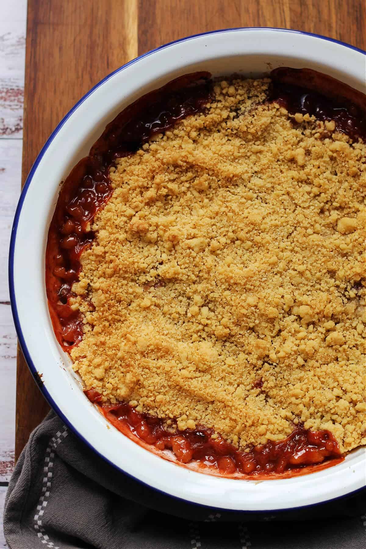 Plum crumble with oozing fruit around the sides of the white pie tin.