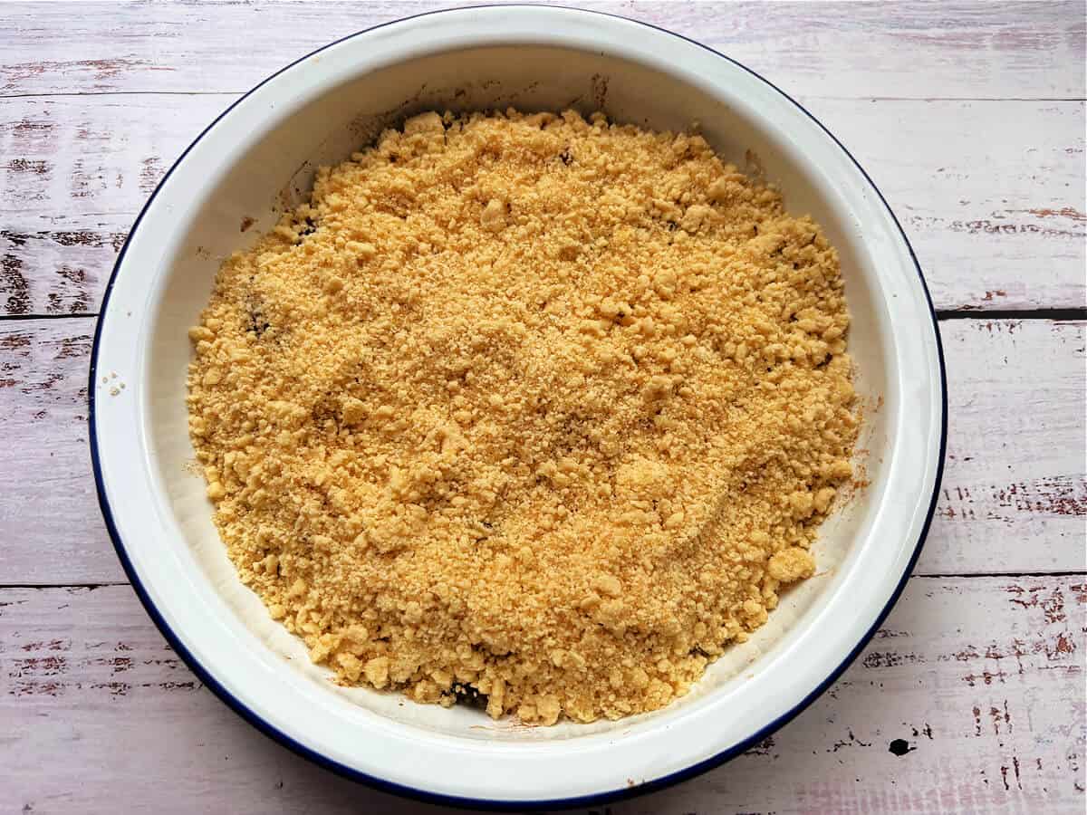 Pie dish with crumble spread over plums.