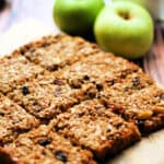 Squares of golden flapjack on a wooden table with apple behind.