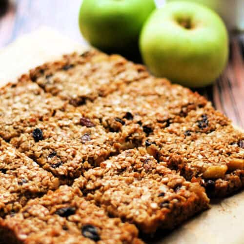 Squares of golden flapjack on a wooden table with apple behind.