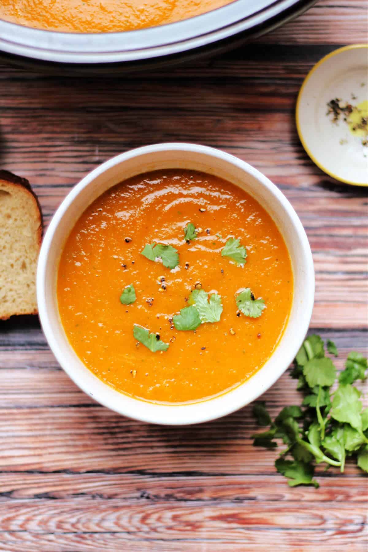 Bowl of carrot soup topped with some coriander leaves.