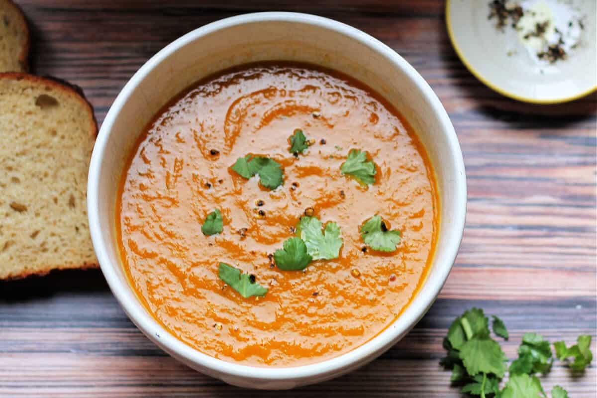 White bowl of carrot soup topped with herbs.