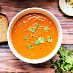 Bowl of carrot and coriander soup topped with chopped coriander leaves.