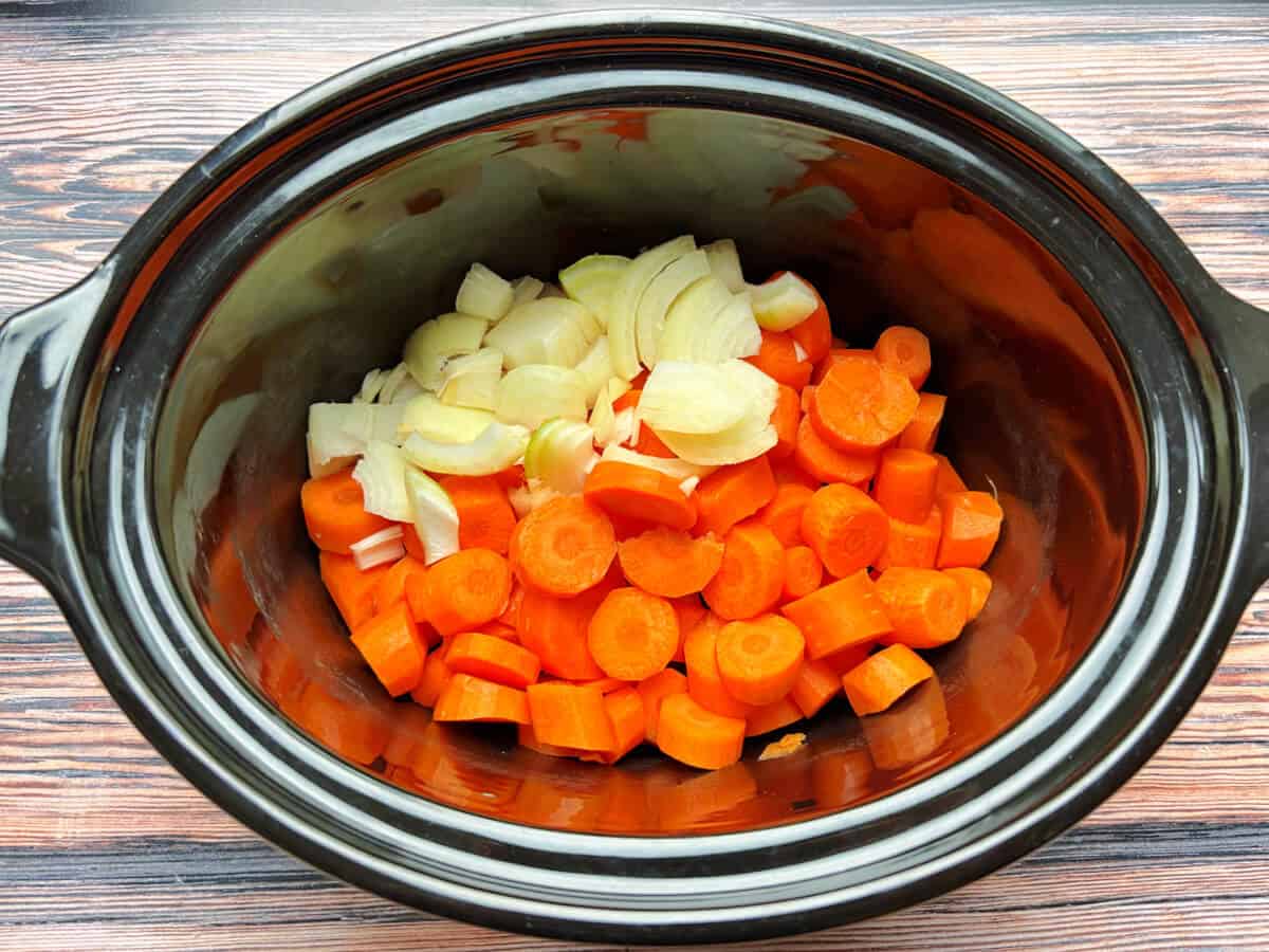 Carrots and onion in a slow cooker pot.