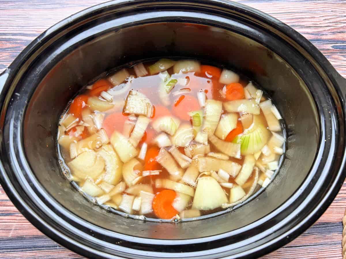 Soup ingredients with stock in slow cooker pot.