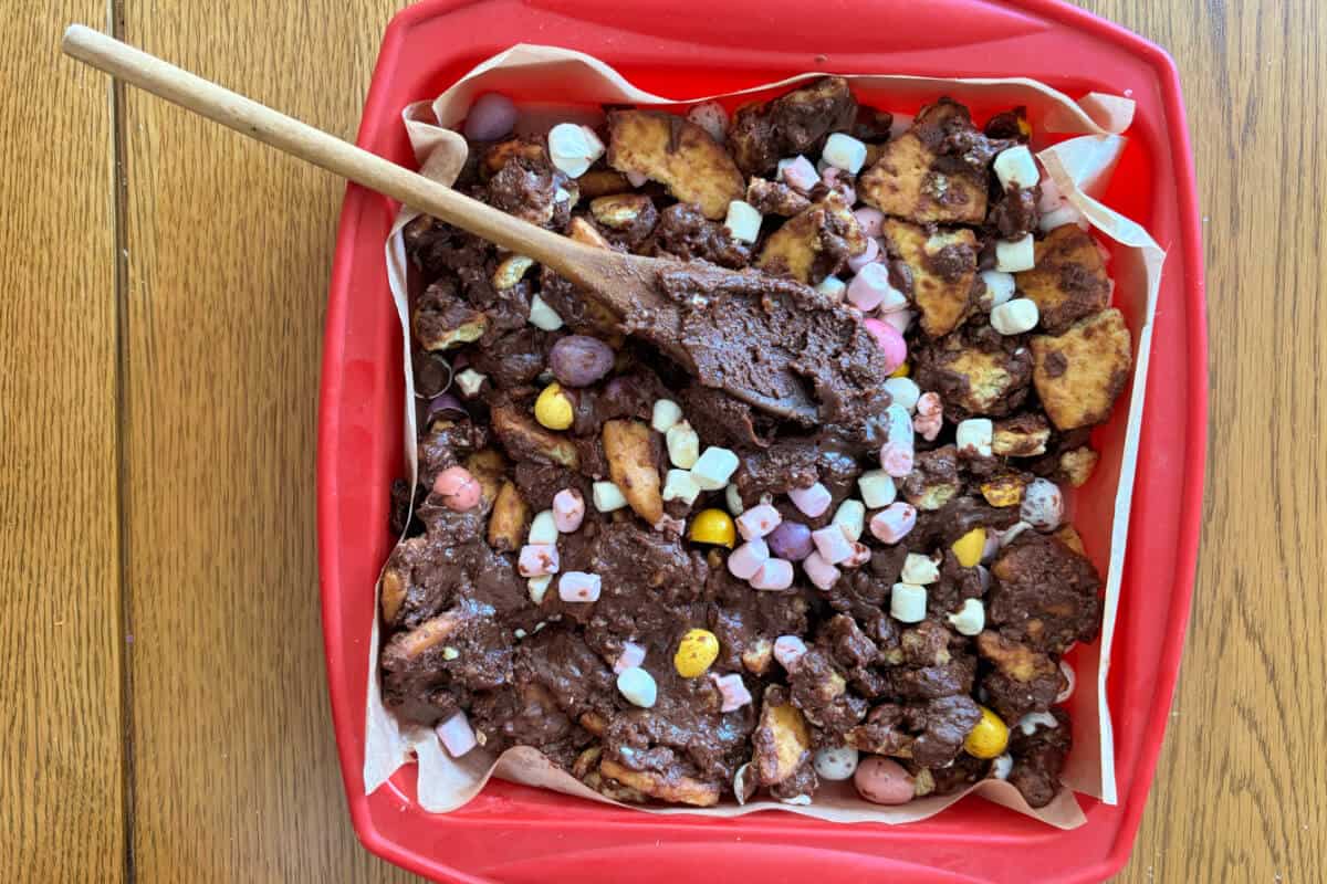 Rocky road ingredients in lined pan, with wooden spoon.