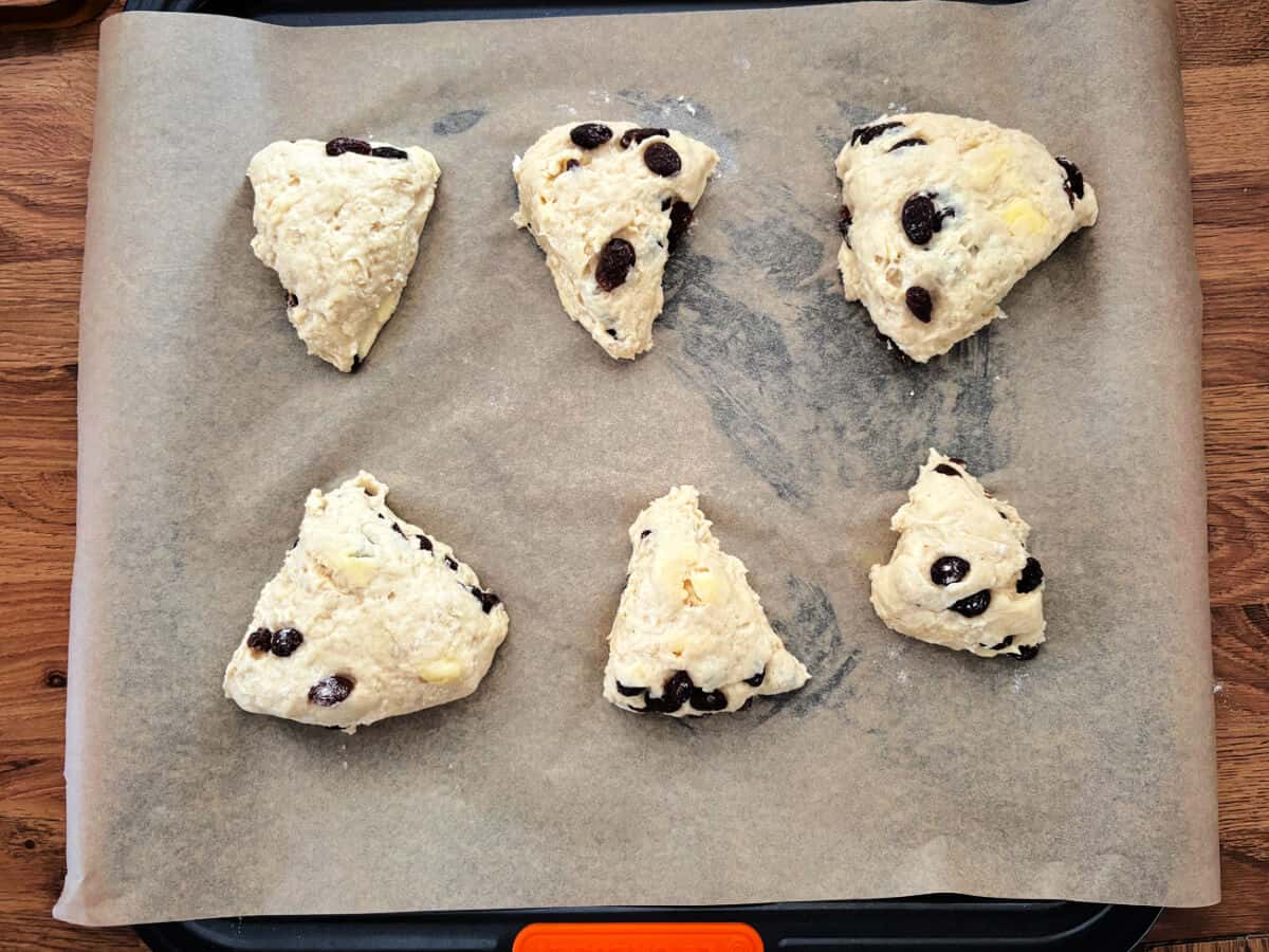 Triangle fruit scones on lined baking tray.