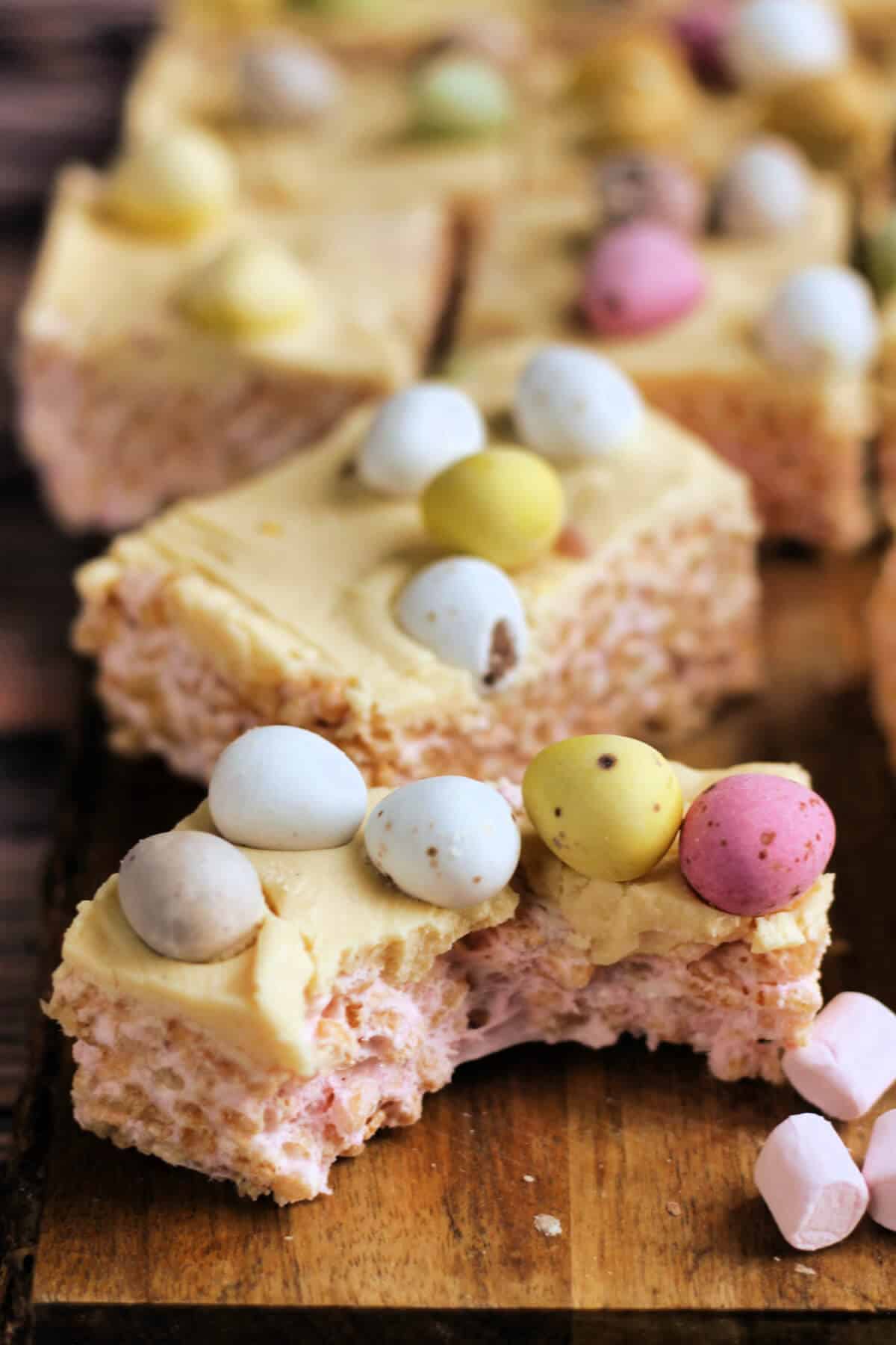 Rice Krispie squares with Mini eggs, one with a bit taken out showing gooey marshmallow.