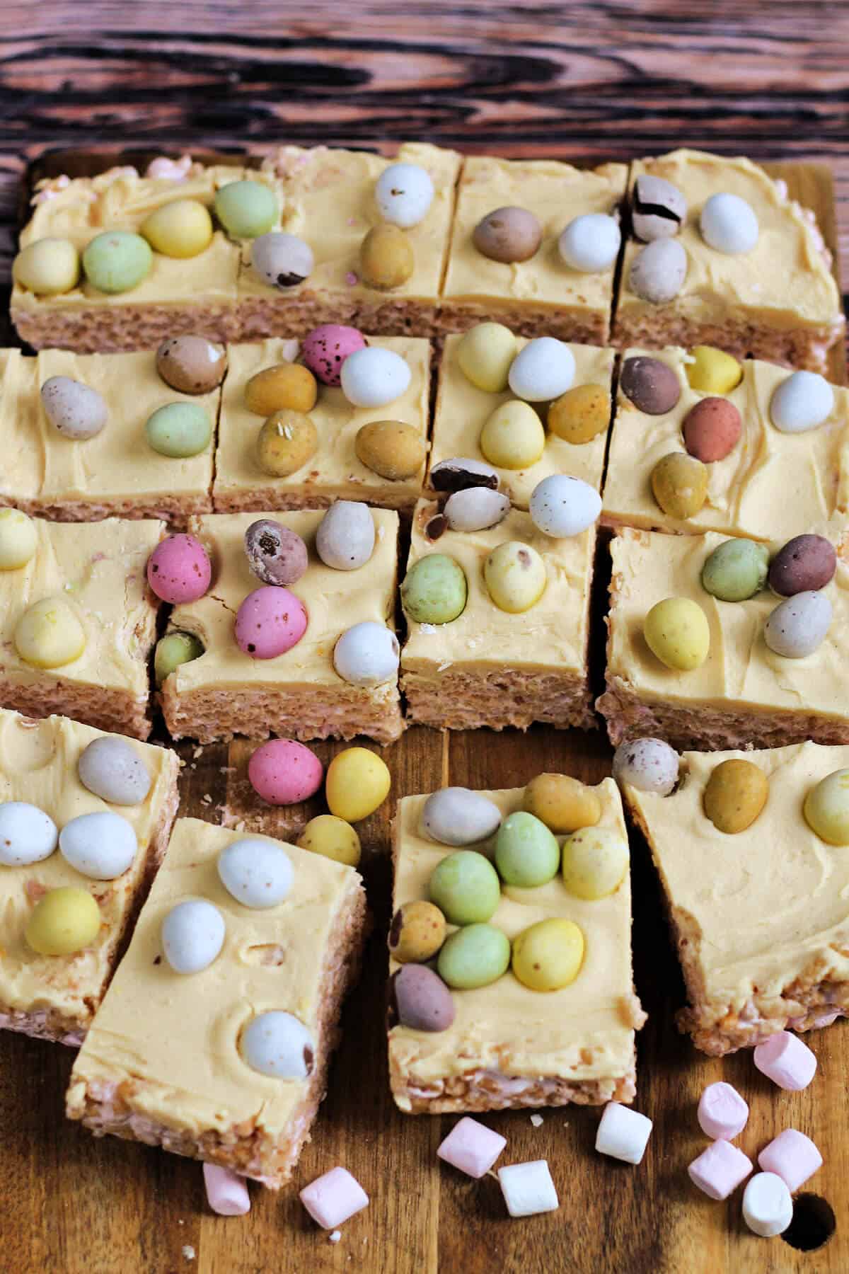 Slab of Rice Krispie treats topped with white chocolate and colourful mini eggs, cut into squares.