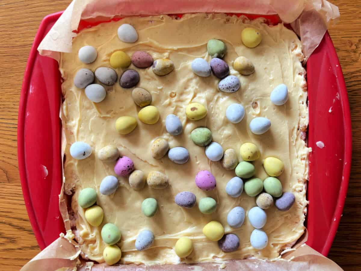 Rice Krispie treats topped with white chocolate with mini eggs added on top, in pan.