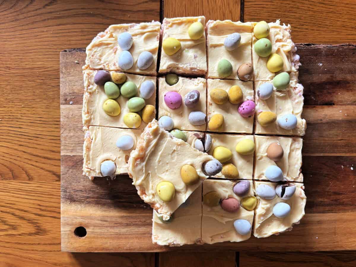 Krispie treats topped with mini eggs cut into squares, on a board.