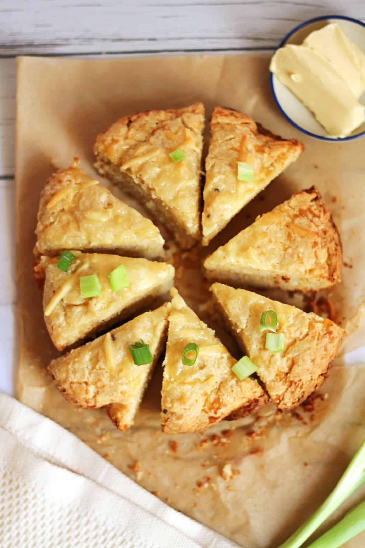 Cheese scone round cut into triangles on baking paper, with scattered spring onion slices.