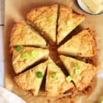 Triange cheese scones in a circle, on baking paper, with scattered spring onion slices.