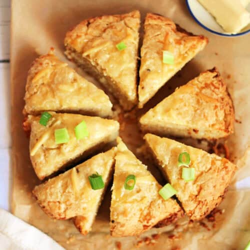 Triange cheese scones in a circle, on baking paper, with scattered spring onion slices.