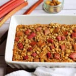 White dish with rhubarb baked oats topped with chunks of rhubarb.