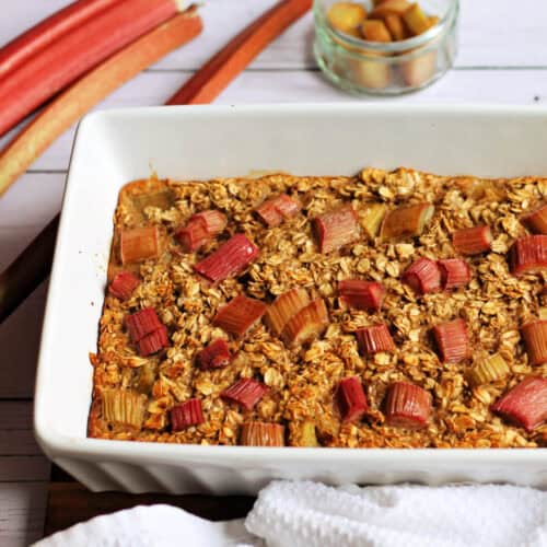 White dish with rhubarb baked oats topped with chunks of rhubarb.