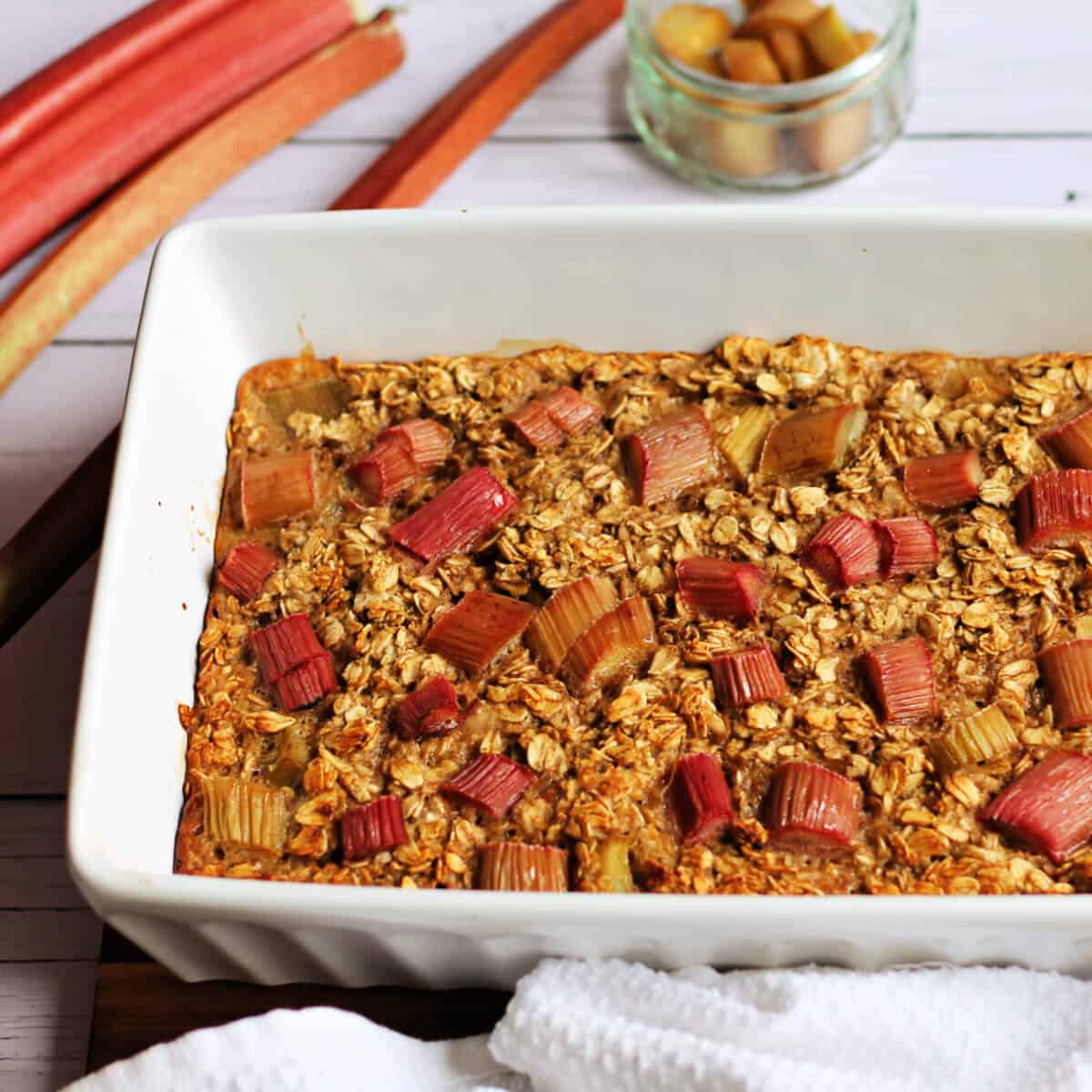 White dish with rhubarb baked oats topped with chunks of rhubarb.