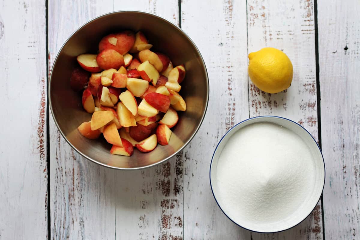Chopped peaches in a bowl, sugar in another bowl and a lemon.